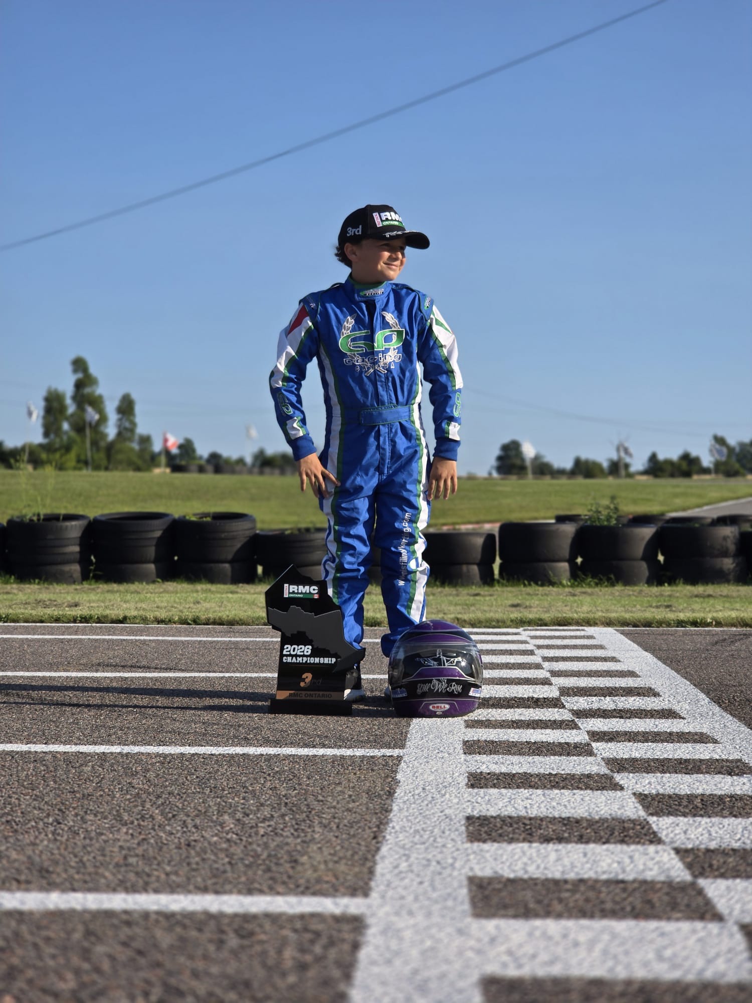 Angelo Launi looking down the track with his RMC Ontario championship trophy and racing helmet
